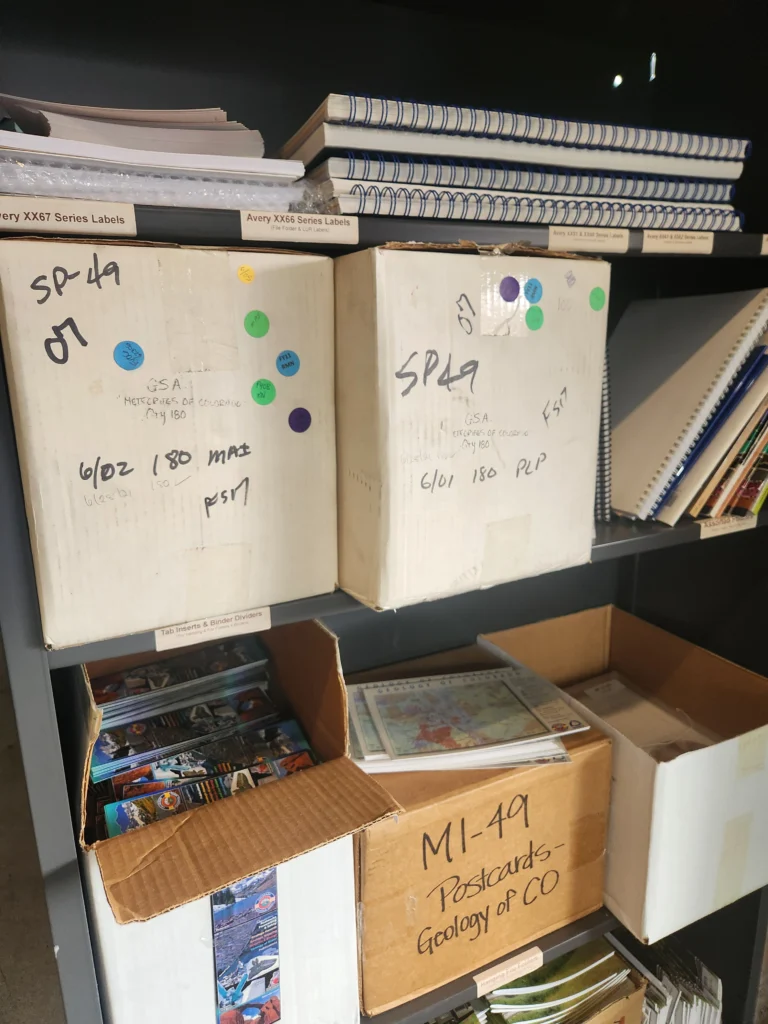 Carboard boxes and books stacked on a metal shelf.