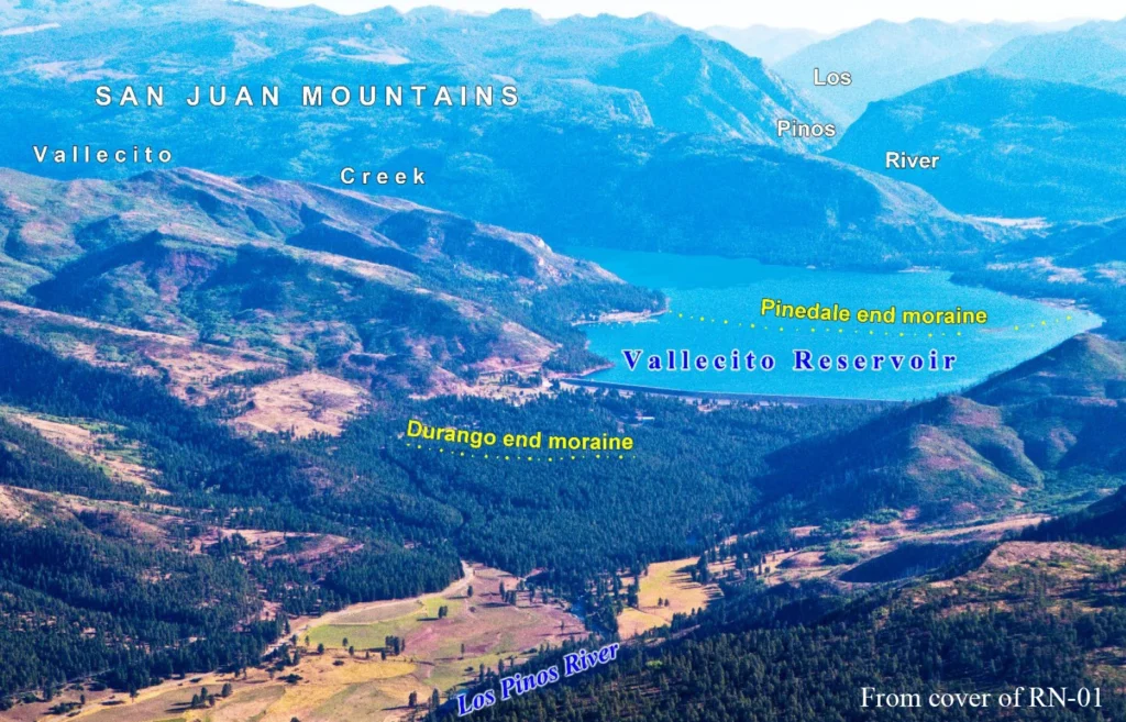 aqua blue reservoir surrounded by heavily forested hills, mountains, with a valley below