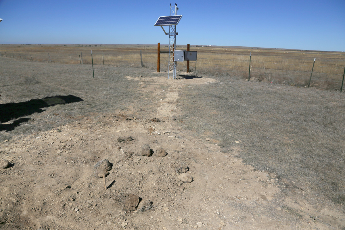 Buried seismometer in foreground with complete PV power and data transmission tower in background, Briggsdale, Colorado, May 2016. Photo credit: Mike Bornowski for the CGS.