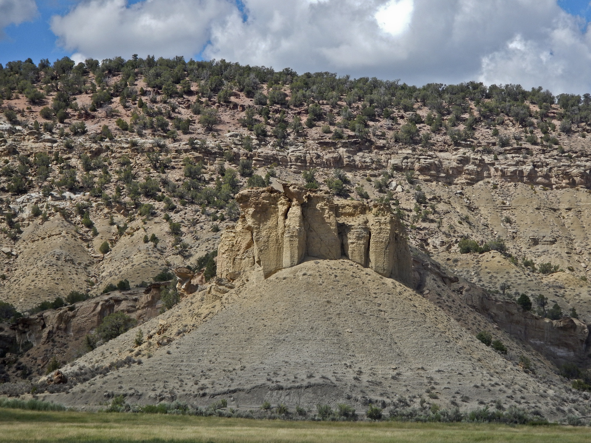 A cuesta along Dirty George Creek capped by Cozzette Sandstone that interfingers the Mancos Shale. The thick whitish colored sandstone in center background above the Mancos is the Rollins Sandstone of the Iles Formation. The reddish rock above is coal-fire clinker in the Williams Fork Cameo coal zone, south of Hells Kitchen, Delta County, Colorado. Photo credit: Jon White for the CGS.