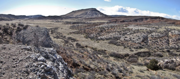 Upper and lower beds of gypsum exposed on the more gently east-dipping limb of the asymmetrical Sand Creek Anticline. Table Mountain in the center background. Sinkholes occur within the small valley in center of image between the chalky-white gypsum beds. Image was taken from the top of the upper gypsum bed. Photo credit: Jon White for the CGS.