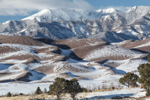 Winter arrives in the San Luis Valley and Sangre de Cristo Range which are separated by a 20,000-foot normal fault. Looking across the less-obvious parabolic dunes in the dried sagebrush to the transverse dunes with reversing crests. The Great Sand Dunes National Park and Preserve claim to hold the highest dune in North America which is the height of a 70-story building—20 stories higher than the tallest building in downtown Denver. The igneous, sedimentary, and metamorphic rocks of the Sangre de Cristo Range exceed 14,000 ft (4267 m) above mean sea level in ten of its peaks, attesting to its young uplift. Photo credit: Vince Matthews.