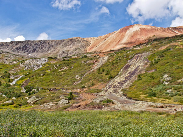 Red Mountain in the Grizzly Peak Caldera feeds acid water into the South Fork of Lake Creek. The foreground slope has ferrosinter deposits (center and right). Ouray County, Colorado. Photo credit: Colorado Geological Survey.